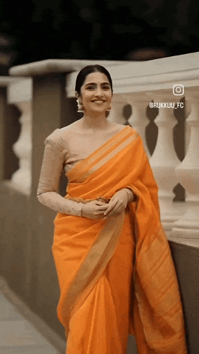 a woman in an orange saree is standing next to a railing .