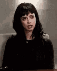 a woman with black hair is sitting at a desk making a face .