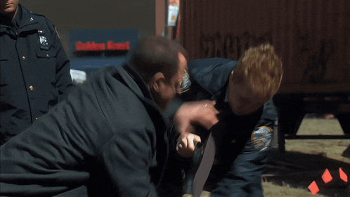 a man in a suit and tie is being held by a police officer with a nyc patch on his jacket