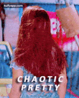 a woman with red hair is standing in front of a sign that says ' chaotic pretty ' on it .