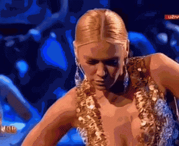 a woman in a gold sequined dress is dancing on a stage in front of a live audience