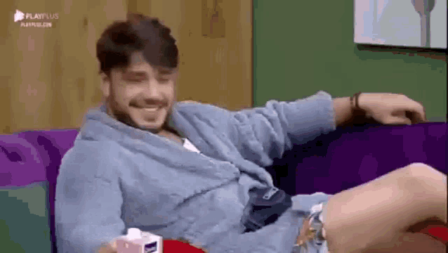 a man in a robe is sitting on a purple couch with his legs crossed .