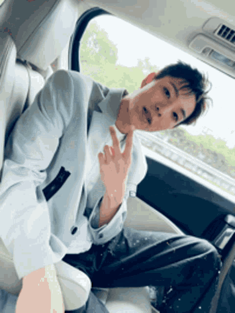 a young man is sitting in the back seat of a car and giving a peace sign