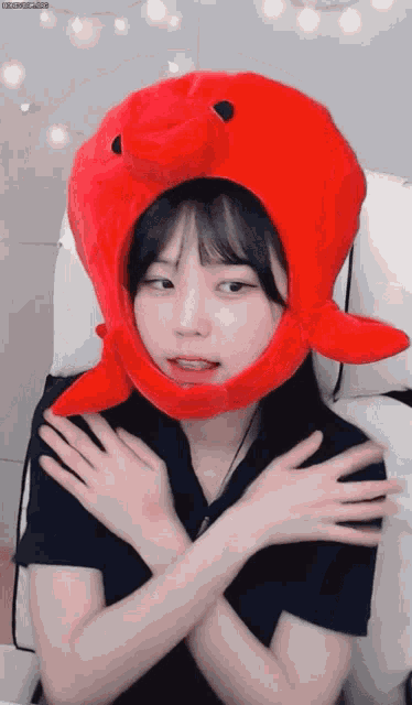 a girl wearing a red octopus hat is sitting with her arms crossed
