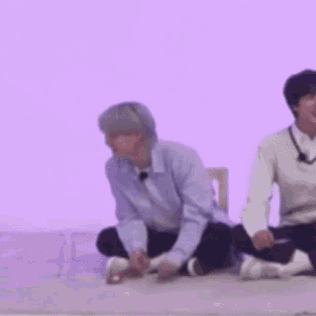 two men are sitting on the floor in front of a purple wall eating ice cream .