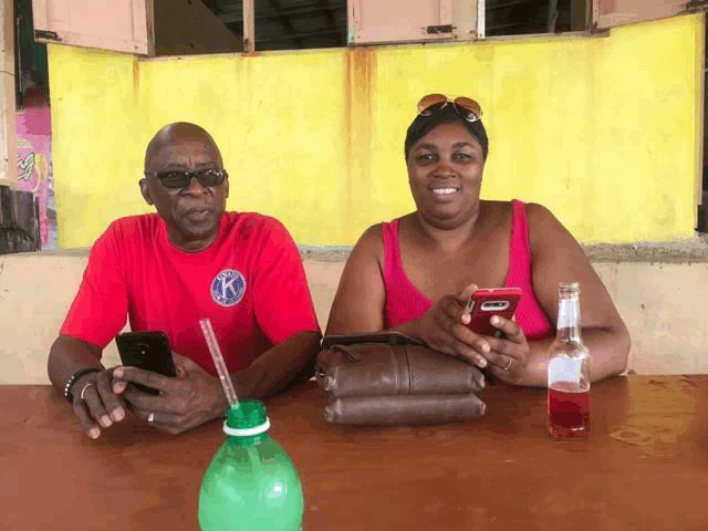 a man and woman sit at a table with a bottle of soda