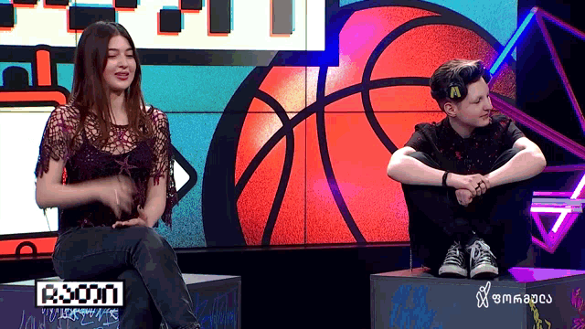 a man and a woman are sitting in front of a basketball and a sign that says r.com
