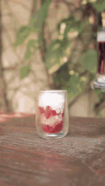 a glass filled with strawberries and whipped cream sits on a table